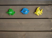 Drie verschillende stuk speelgoed vissen van groene, blauwe en gele kleuren op de houten vloer van een houten buitenhuis Horizont stock foto Drie verschillende stuk speelgoed vissen van groene, blauwe en gele kleuren op de houten vloer van een houten buitenhuis Horizont stock foto