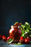 Dried tomatoes in olive oil with green basil and spices in glass jar on blue kitchen table, place for text stock photography Dried tomatoes in olive oil with green basil and spices in glass jar on blue kitchen table, place for text stock photography