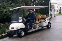Driver of a tourist electric golf cart in a Christmas hat looks into a smartphone and smiles in his free time in the park