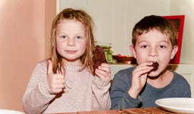Duas crianças estão comendo cookies que marrons a menina está dando o thum acima Conceito engraçado e das crianças Adicione o efe foto de stock royalty free Duas crianças estão comendo cookies que marrons a menina está dando o thum acima Conceito engraçado e das crianças Adicione o efe foto de stock royalty free