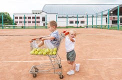Duas crianças que jogam no campo de tênis Bolas do rapaz pequeno e de tênis no carrinho de compras fotos de stock royalty free Duas crianças que jogam no campo de tênis Bolas do rapaz pequeno e de tênis no carrinho de compras fotos de stock royalty free