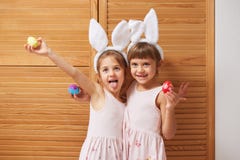 Duas irmãs mais nova encantadores engraçadas nos vestidos com as orelhas de coelho brancas em suas cabeças guardam ovos tingidos imagem de stock royalty free Duas irmãs mais nova encantadores engraçadas nos vestidos com as orelhas de coelho brancas em suas cabeças guardam ovos tingidos imagem de stock royalty free