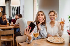 Duas meninas positivas que sorriem e que fazem o selfie com vinho no restaurante imagens de stock royalty free Duas meninas positivas que sorriem e que fazem o selfie com vinho no restaurante imagens de stock royalty free