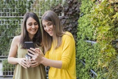 Duas mulheres bonitas que tomam o selfie com telefone celular Fundo verde Um está guardando uma xícara de café Estão rindo e fotografia de stock royalty free Duas mulheres bonitas que tomam o selfie com telefone celular Fundo verde Um está guardando uma xícara de café Estão rindo e fotografia de stock royalty free