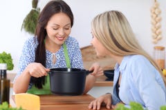 Duas mulheres felizes novas estão cozinhando na cozinha Os amigos estão tendo o divertimento ao preapering a refeição saudável e foto de stock royalty free Duas mulheres felizes novas estão cozinhando na cozinha Os amigos estão tendo o divertimento ao preapering a refeição saudável e foto de stock royalty free
