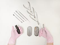 Duas mãos fêmeas nas luvas Verniz para as unhas e tenazes de brasa nas mãos Ferramentas para o tratamento de mãos Fundo branco, v Imagem de Stock Duas mãos fêmeas nas luvas Verniz para as unhas e tenazes de brasa nas mãos Ferramentas para o tratamento de mãos Fundo branco, v Imagem de Stock