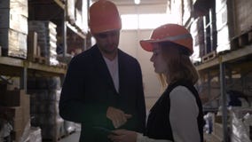 Due colleghe in caschi duri al magazzino che discutono lavoro con le mani del computer e di scossa della compressa video d archivio Due colleghe in caschi duri al magazzino che discutono lavoro con le mani del computer e di scossa della compressa video d archivio