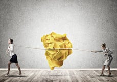 Due donne che tirano con la grande palla sgualcita di sforzo di carta come creatività firmano immagine stock Due donne che tirano con la grande palla sgualcita di sforzo di carta come creatività firmano immagine stock