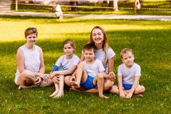 Due donne e tre bambini si siedono su erba verde fotografia stock Due donne e tre bambini si siedono su erba verde fotografia stock