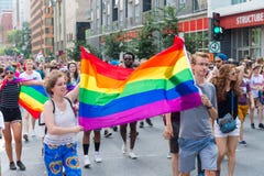 Due giovani che tengono una grande bandiera gay dell'arcobaleno immagini stock Due giovani che tengono una grande bandiera gay dell'arcobaleno immagini stock