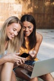 Due ragazze sorridenti che per mezzo del computer portatile al parco immagini stock Due ragazze sorridenti che per mezzo del computer portatile al parco immagini stock