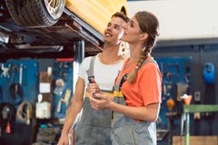 Dwa dedykowali auto mechaników ono uśmiecha się podczas gdy sprawdzać koła samochód Obraz Stock Dwa dedykowali auto mechaników ono uśmiecha się podczas gdy sprawdzać koła samochód Obraz Stock
