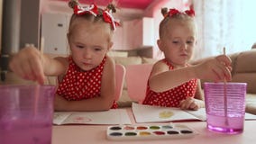 Dwa małych siostr bliźniaka siedzi przy stołem wpólnie są szczęśliwi malować rysunki z akwarelami Dwa małych siostr bliźniaka siedzi przy stołem wpólnie są szczęśliwi malować rysunki z akwarelami