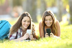 Dwa ucznia texting w ich mądrze telefonach w parku zdjęcie stock Dwa ucznia texting w ich mądrze telefonach w parku zdjęcie stock