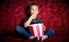 Dziecka kino: Troszkę chłopiec, preschooler, ogląda film na dużej czerwonej kanapie w domu i je popkorn od dużego obrazy stock Dziecka kino: Troszkę chłopiec, preschooler, ogląda film na dużej czerwonej kanapie w domu i je popkorn od dużego obrazy stock