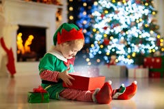 Dziecka otwarcie teraźniejszy przy choinką w domu Dzieciak w elfa kostiumu z Xmas zabawkami i prezentami fotografia stock Dziecka otwarcie teraźniejszy przy choinką w domu Dzieciak w elfa kostiumu z Xmas zabawkami i prezentami fotografia stock