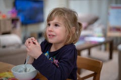 Dziewczyny obsiadanie przy śniadaniowym łasowania muesli z yoghourt od białego pucharu obrazy stock Dziewczyny obsiadanie przy śniadaniowym łasowania muesli z yoghourt od białego pucharu obrazy stock