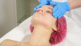 Beauticians w niebieskich rękawiczkach nakłada śmietanę na twarz młodych kobiet Koncepcja naprawy i odmłodzenia twarzy Zamykanie zdjęcie wideo Beauticians w niebieskich rękawiczkach nakłada śmietanę na twarz młodych kobiet Koncepcja naprawy i odmłodzenia twarzy Zamykanie zdjęcie wideo