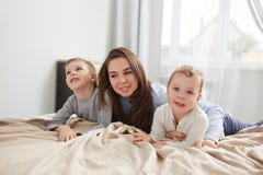 E Молодая мать одетая в светлом - голубая пижама кладет с ее 2 маленькими сыновьями на кровать с бежевым одеялом внутри стоковое фото rf E Молодая мать одетая в светлом - голубая пижама кладет с ее 2 маленькими сыновьями на кровать с бежевым одеялом внутри стоковое фото rf