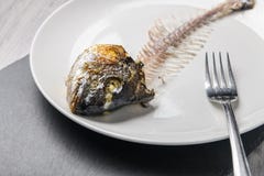 Eaten fish skeleton on the white plate on gray wooden table. Concept for food shortage and misery. Close up view