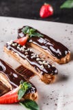 Eclairs caseiros ou profiteroles do bolo com creme, chocolate e morangos no fundo escuro servido com x?cara de caf? imagens de stock Eclairs caseiros ou profiteroles do bolo com creme, chocolate e morangos no fundo escuro servido com x?cara de caf? imagens de stock