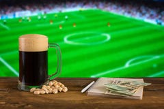 Een glas donker bier, pistachioson met blocnote en dollarrekeningen op de achtergrond van voetbalstadion Met exemplaarruimte royalty-vrije stock fotografie Een glas donker bier, pistachioson met blocnote en dollarrekeningen op de achtergrond van voetbalstadion Met exemplaarruimte royalty-vrije stock fotografie