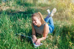 Een jong meisje maakt aankopen die in de online opslag door de computer op het groene gras liggen stock foto Een jong meisje maakt aankopen die in de online opslag door de computer op het groene gras liggen stock foto