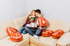 Een jong paar in liefde, een man wenst een vrouw door haar een boeket van tulpen en een gift geluk te geven, thuis zittend met de royalty-vrije stock fotografie Een jong paar in liefde, een man wenst een vrouw door haar een boeket van tulpen en een gift geluk te geven, thuis zittend met de royalty-vrije stock fotografie