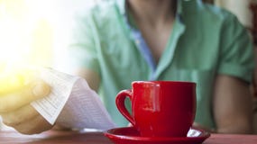Een jonge mens onderzoekt de rekening in een koffie op een Zonnige de zomerochtend stock foto's Een jonge mens onderzoekt de rekening in een koffie op een Zonnige de zomerochtend stock foto's