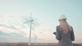 Een jonge onderneemster in een helm is op de plaats tegen de windmolen Bouwvak voor jongeren E stock video Een jonge onderneemster in een helm is op de plaats tegen de windmolen Bouwvak voor jongeren E stock video