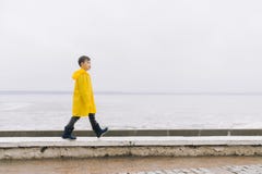 Een jongen in een gele mantelregenjas loopt langs de kust G royalty-vrije stock afbeeldingen Een jongen in een gele mantelregenjas loopt langs de kust G royalty-vrije stock afbeeldingen