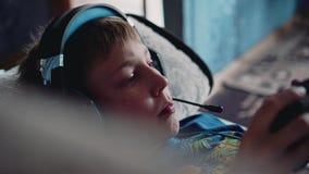 Een jongen met een hoofdtelefoon op zijn hoofd in een videospelletje die op de laag liggen Hij houdt een controlemechanisme Pret stock footage Een jongen met een hoofdtelefoon op zijn hoofd in een videospelletje die op de laag liggen Hij houdt een controlemechanisme Pret stock footage