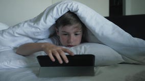 Een jongensclose-up let op beeldverhalen op een digitale tablet bij nacht onder een deken Concept elektronische verslaving stock footage Een jongensclose-up let op beeldverhalen op een digitale tablet bij nacht onder een deken Concept elektronische verslaving stock footage