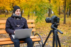 Een kerelzitting op een bank tegenover de camera en het gebruiken van laptop In het de herfstpark stock foto's Een kerelzitting op een bank tegenover de camera en het gebruiken van laptop In het de herfstpark stock foto's