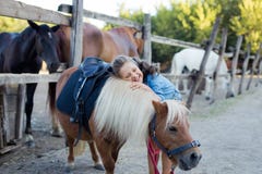 Een klein glimlachend meisje met krullend haar kleedde zich in jeans koesterend met een poney bij de stal royalty-vrije stock fotografie Een klein glimlachend meisje met krullend haar kleedde zich in jeans koesterend met een poney bij de stal royalty-vrije stock fotografie