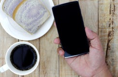Een kop van koffie, brood op witte plaat, smartphone streeft ter beschikking na stock afbeelding Een kop van koffie, brood op witte plaat, smartphone streeft ter beschikking na stock afbeelding