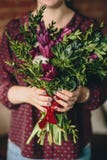 Een meisje in een blouse van Bourgondië houdt een boeket van tulpen, bukshout en installaties met een manicure stock foto's Een meisje in een blouse van Bourgondië houdt een boeket van tulpen, bukshout en installaties met een manicure stock foto's