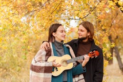 Een meisje met een ukelele in haar handen bekijkt de kerel naast een de herfstachtergrond stock fotografie Een meisje met een ukelele in haar handen bekijkt de kerel naast een de herfstachtergrond stock fotografie