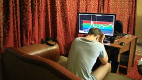 Een mens in een T-shirt en borrels, die thuis op de laag de zitten, controleren veranderingen in het programma op de muntuitwisse stock videobeelden Een mens in een T-shirt en borrels, die thuis op de laag de zitten, controleren veranderingen in het programma op de muntuitwisse stock videobeelden