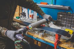 Een mensenarbeider herstelt in de workshop van de skidienst de het glijden oppervlakte van de skis, Basis het oppoetsen, het defi royalty-vrije stock foto Een mensenarbeider herstelt in de workshop van de skidienst de het glijden oppervlakte van de skis, Basis het oppoetsen, het defi royalty-vrije stock foto