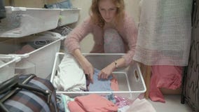 Een mooi meisje, een jonge moeder neemt en vouwt de kleren van kinderen in manden in haar kleedkamer op brengt dingen aan stock footage Een mooi meisje, een jonge moeder neemt en vouwt de kleren van kinderen in manden in haar kleedkamer op brengt dingen aan stock footage