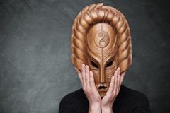 Een persoon die houten masker dragen die yin yang harmonie symboliseren die zijn handen op het masker houden die zich over grijze royalty-vrije stock foto's Een persoon die houten masker dragen die yin yang harmonie symboliseren die zijn handen op het masker houden die zich over grijze royalty-vrije stock foto's