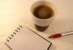 Een A5 rangschikte spiraalvormig notitieboekje, een ballpoint en een kop van koffie op witte kantachtergrond royalty-vrije stock foto's Een A5 rangschikte spiraalvormig notitieboekje, een ballpoint en een kop van koffie op witte kantachtergrond royalty-vrije stock foto's
