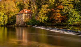 Een rivier kruist een waterkering, met een achtergrond van een huis & de herfstbomen royalty-vrije stock afbeelding Een rivier kruist een waterkering, met een achtergrond van een huis & de herfstbomen royalty-vrije stock afbeelding