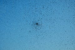Ein Einschussloch in einer Glasnahaufnahme auf einem blauen Hintergrund stockfoto Ein Einschussloch in einer Glasnahaufnahme auf einem blauen Hintergrund stockfoto