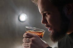 Ein ernster Kerl mit einem Bart hält ein Glas Kolabaum oder Whisky mit Eis in seiner Hand Steuern Sie das modellieren des Lichtes lizenzfreies stockbild Ein ernster Kerl mit einem Bart hält ein Glas Kolabaum oder Whisky mit Eis in seiner Hand Steuern Sie das modellieren des Lichtes lizenzfreies stockbild