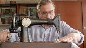 Ein erwachsener Mann mit einem Schnurrbart näht auf einer alten hand-genähten Maschine Gläser werden gekleidet und weißer Stoff w stock video footage Ein erwachsener Mann mit einem Schnurrbart näht auf einer alten hand-genähten Maschine Gläser werden gekleidet und weißer Stoff w stock video footage
