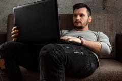Ein junger Mann, der an einem Laptop zu Hause sich entspannt auf einer bequemen Couch in den Jeans arbeitet Das Konzept des Freib stockbilder Ein junger Mann, der an einem Laptop zu Hause sich entspannt auf einer bequemen Couch in den Jeans arbeitet Das Konzept des Freib stockbilder