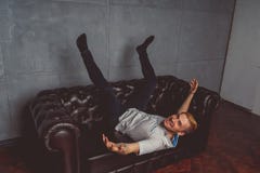 Ein junger Mann mit einer Tätowierung auf seiner Hand, die auf einer Ledercouch aufwirft Straßenartkleidung: weißes Hemd und schw lizenzfreie stockfotos Ein junger Mann mit einer Tätowierung auf seiner Hand, die auf einer Ledercouch aufwirft Straßenartkleidung: weißes Hemd und schw lizenzfreie stockfotos
