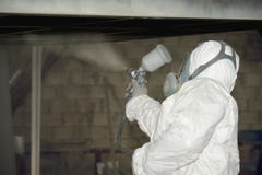 Ein Mann in einer wei?en Uniform wendet Farbe mit einer Farbspritzpistole auf einem Metallprodukt an lizenzfreies stockbild Ein Mann in einer wei?en Uniform wendet Farbe mit einer Farbspritzpistole auf einem Metallprodukt an lizenzfreies stockbild